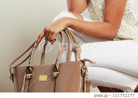 Woman holding beige lacquered leather bag. 111752277