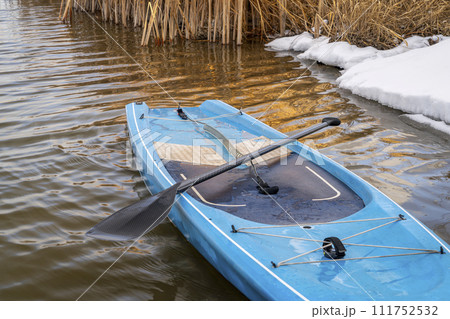 touring stand up paddleboard with a paddle and safety leash on a shore of lake in northern Colorado, winter or early spring scenery with some snow touring stand up paddleboard with a paddle and safety leash on a shore of lake in northern Colorado, winter or early spring scenery with some snow 111752532