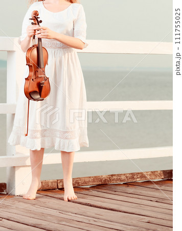 Woman on pier outside holding violin 111755025
