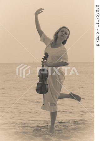 Woman on beach near sea holding violin Woman on beach near sea holding violin 111755030