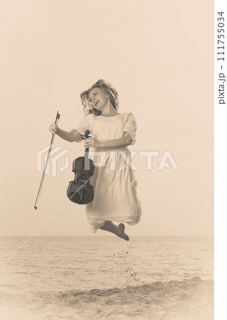 Woman on beach near sea holding violin Woman on beach near sea holding violin 111755034