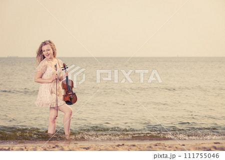Woman on beach near sea holding violin Woman on beach near sea holding violin 111755046
