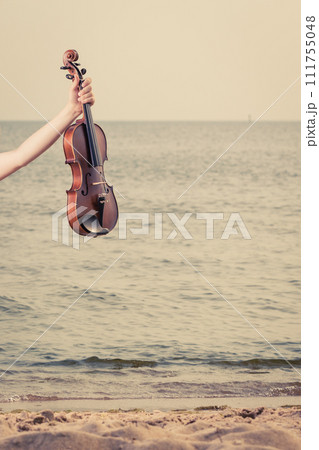 Woman on beach near sea holding violin Woman on beach near sea holding violin 111755048