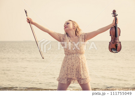 Woman on beach near sea holding violin Woman on beach near sea holding violin 111755049