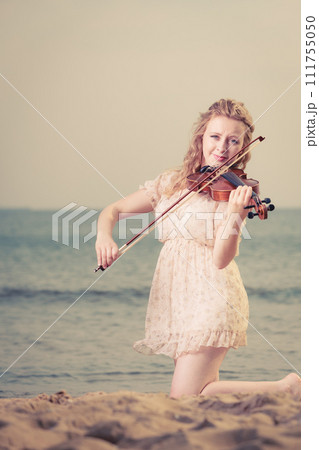 Woman on beach near sea holding violin Woman on beach near sea holding violin 111755050