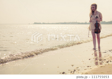 Woman on beach near sea holding violin Woman on beach near sea holding violin 111755053