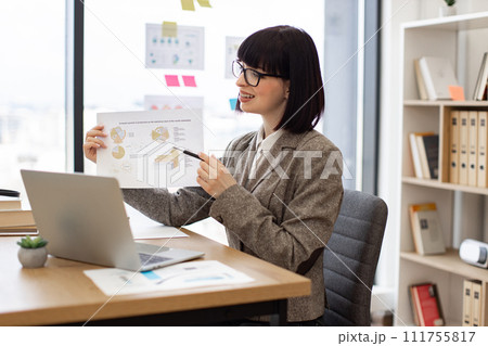Caucasian woman pointing at document with infographics of online presentation. Caucasian woman pointing at document with infographics of online presentation. 111755817