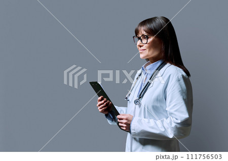 Profile portrait of female doctor holding clipboard on gray background, copy space 111756503