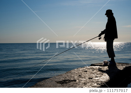 silhouette of a fisherman catches fish at sea silhouette of a fisherman catches fish at sea 111757017