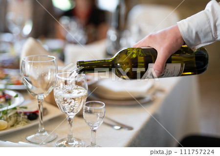 the waiter pours an alcoholic drink, wine into a glass the waiter pours an alcoholic drink, wine into a glass 111757224