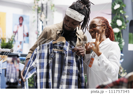 Smiling influencers recording shirt review video while showing ok sign with fingers. Cheerful african american blogger and clothing store assistant showcasing fashion brand for online followers Smiling influencers recording shirt review video while showing ok sign with fingers. Cheerful african american blogger and clothing store assistant showcasing fashion brand for online followers 111757345