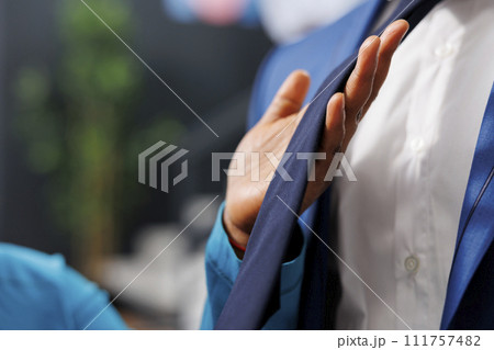 Woman holding stylish tie, analyzing clothes material during shopping session in modern boutique. African american customer looking to buy formal merchandise and accessories. Close up Woman holding stylish tie, analyzing clothes material during shopping session in modern boutique. African american customer looking to buy formal merchandise and accessories. Close up 111757482