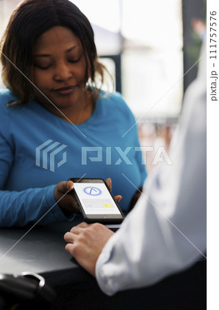 African american shopper buying clothes with phone nfc payment, using smartphone at pos terminal in modern boutique store. Woman paying for fashionable casual wear and accessories at counter. Close up African american shopper buying clothes with phone nfc payment, using smartphone at pos terminal in modern boutique store. Woman paying for fashionable casual wear and accessories at counter. Close up 111757576