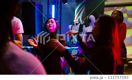 Young persons dancing at club, having fun at disco party on dance floor with funky music. Cheerful group of friends enjoying social gathering at discotheque, colorful lights. Handheld shot. Young persons dancing at club, having fun at disco party on dance floor with funky music. Cheerful group of friends enjoying social gathering at discotheque, colorful lights. Handheld shot. 111757593