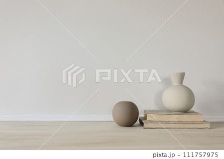 Set of modern brown and beige ceramic vases of geometric shapes on wooden table. Old books. White wall. Abstract trendy artistic background, web banner. Empty copy space. Elegant interior. 111757975