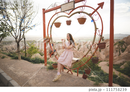 Girl sitting on a decorated heart-shaped bench on a viewpoint and admiring view of Cappadocia 111758239