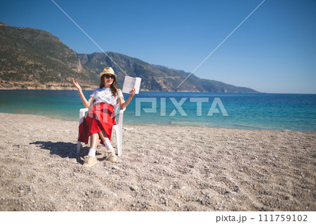 happy girl in a red skirt on an empty beach sits on a chair and reads a book happy girl in a red skirt on an empty beach sits on a chair and reads a book 111759102