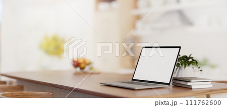 A laptop computer mockup on a wooden kitchen island tabletop in a modern bright kitchen. 111762600