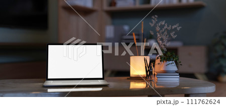 A home workspace at night with a white-screen laptop computer mockup on a marble coffee table 111762624