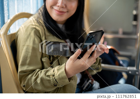 A smiling Asian female passenger is using her smartphone while sitting in a bus. A smiling Asian female passenger is using her smartphone while sitting in a bus. 111762851