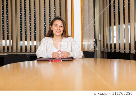 Young latin american businesswoman sitting with briefcase in meeting room Young latin american businesswoman sitting with briefcase in meeting room 111763256