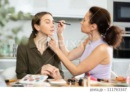 Woman applying soft shade of eyeshadow to friend eyelids 111763387