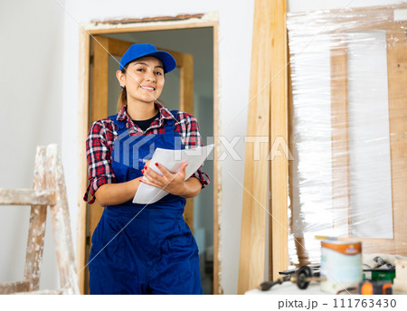 Positive woman builder with documents in apartment 111763430