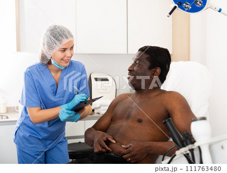 Cosmetician with papers talking to man before procedure in clinic 111763480