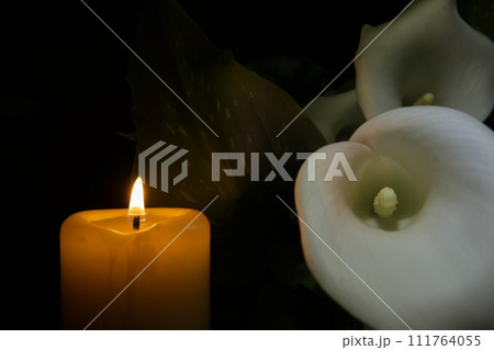 Burning wax candle and white calla lily flowers in darkness 111764055