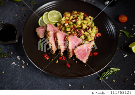 Sliced Organic grilled Tuna fillet covered with sesame seeds and salsa on black ceramic plate Sliced Organic grilled Tuna fillet covered with sesame seeds and salsa on black ceramic plate 111768125