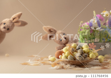 Easter eggs, feathers, spring flowers, and toy bunny on a beige background. Easter eggs, feathers, spring flowers, and toy bunny on a beige background. 111768456