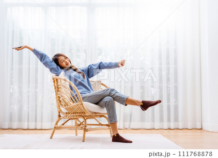 Young Asian Woman Relaxing in Modern Wicker Chair Near Window with Sheer Curtain 111768878