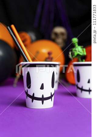 Halloween party. Cup with straws on the table with skeletons and balloons in the background Halloween party. Cup with straws on the table with skeletons and balloons in the background 111771833