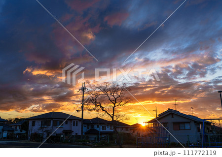 早春の住宅街を照らす夕焼け空　黄金色の空に浮かぶ夕焼け雲と青空のグラデーション　住宅街に沈む夕日 111772119