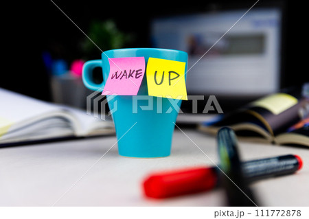 Sticky notes on a coffe cup at office desk. Wake up. Prepare for work Sticky notes on a coffe cup at office desk. Wake up. Prepare for work 111772878
