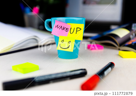 Sticky notes on a coffe cup at office desk. Wake up and smile. Begin your day with Positive thoughts Sticky notes on a coffe cup at office desk. Wake up and smile. Begin your day with Positive thoughts 111772879