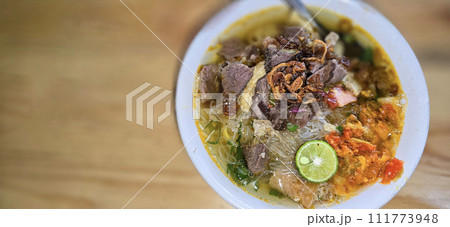 Indonesian style beef noodle soup called soto mie, freshly made soup with vermicelli rice noodle, fried shallots, chilli paste, and fried rissoles Indonesian style beef noodle soup called soto mie, freshly made soup with vermicelli rice noodle, fried shallots, chilli paste, and fried rissoles 111773948