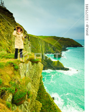 Irish atlantic coast. Woman tourist standing on rock cliff Irish atlantic coast. Woman tourist standing on rock cliff 111775891