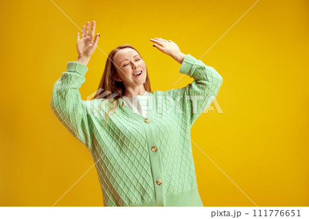 Portrait of young positive woman dancing raised hands up of joy and happiness against yellow studio background. Concept of human emotions. Portrait of young positive woman dancing raised hands up of joy and happiness against yellow studio background. Concept of human emotions. 111776651