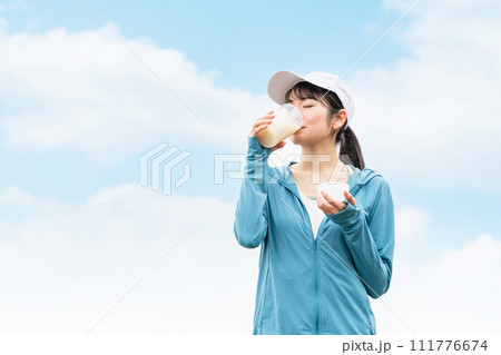 ボディメイクのため公園でプロテインを飲みながらトレーニングするスポーツウェアのアジア人女性 111776674