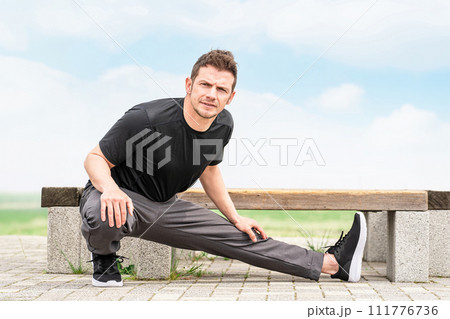 公園で運動前の準備運動・ウォーミングアップで屈伸するスポーツウェアの白人男性 111776736