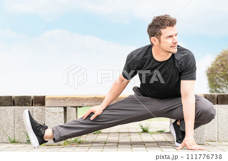 公園で運動前の準備運動・ウォーミングアップで屈伸するスポーツウェアの白人男性 公園で運動前の準備運動・ウォーミングアップで屈伸するスポーツウェアの白人男性 111776738
