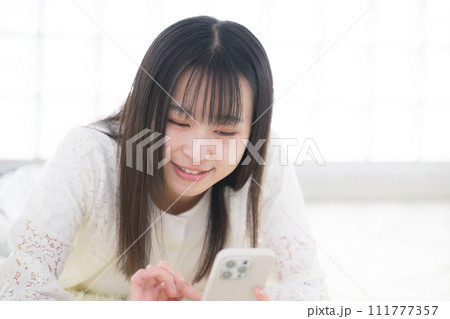 寝転がってスマホを操作する女性 寝転がってスマホを操作する女性 111777357