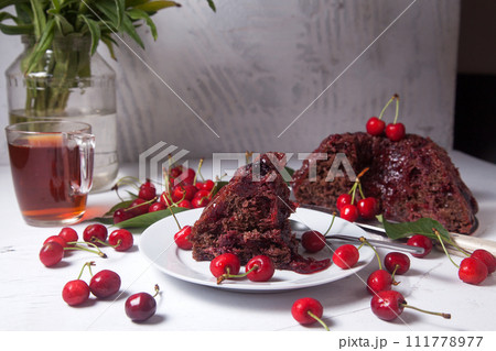 Chocolate cake with sweet cherry, cup of tea and bouquet of blue flowers on white background.. 111778977