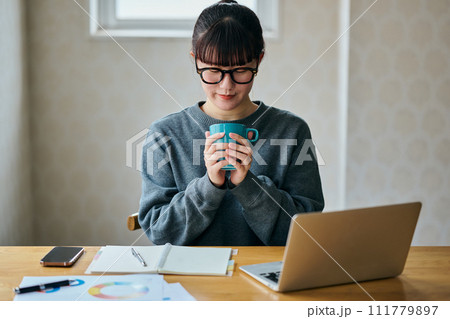 両手でコーヒーカップを持ちくつろぐ若い女性 111779897