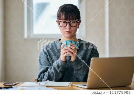 両手でコーヒーカップを持ちぼーっとする若い女性 111779908