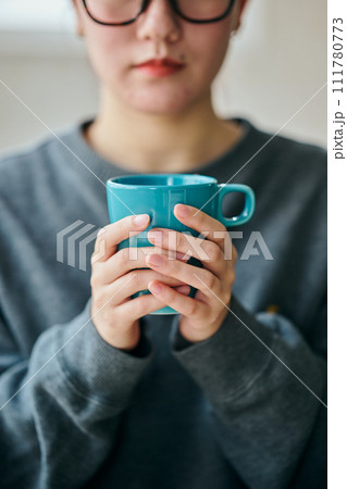 両手でコーヒーカップを持ちくつろぐ若い女性 111780773