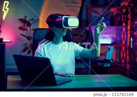 Young woman, influencer, blogger wearing VR glasses, checking modern gadgets possibilities, doing unpacking for followers 111781169