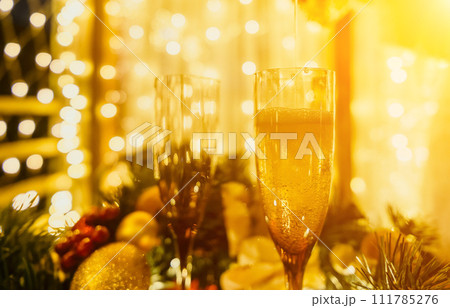 Two champagne glasses filled with champagne are placed on a table with a fruit arrangement. The glasses are surrounded by lights, creating a festive atmosphere. 111785276