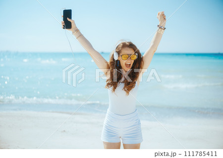 happy stylish female on seashore with headphones dancing happy stylish female on seashore with headphones dancing 111785411